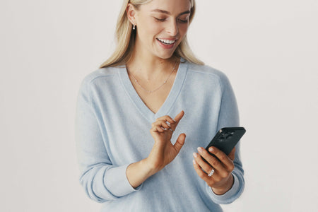 Model wearing white gold and diamond jewellery and holding a phone browsing.